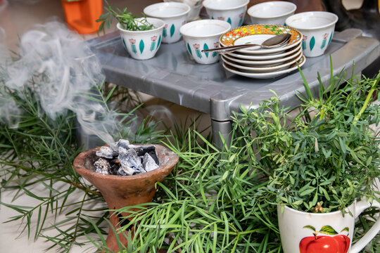 A jebena sits on a grass-covered table with small, handle-less cups arranged around it. Roasted coffee beans, a mortar and pestle, and incense smoke create a traditional Ethiopian coffee ceremony