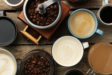 Different coffee drinks in cups, beans and manual grinder on wooden table, flat lay