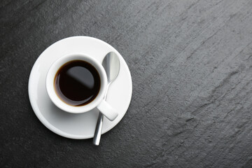 Hot coffee in cup, spoon and saucer on dark textured table, top view. Space for text
