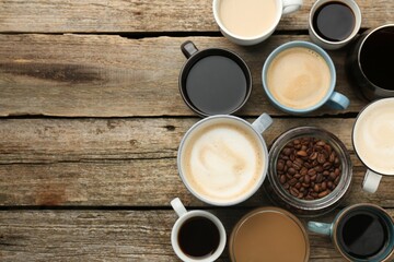 Different coffee drinks in cups and beans on wooden table, flat lay. Space for text