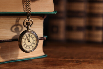 Pocket clock hanging on stack of books at wooden table, closeup. Space for text