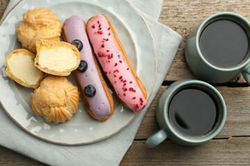 Aromatic coffee in cups, tasty eclairs and profiteroles on wooden table, top view