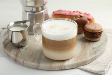 Aromatic coffee in cup, milk, tasty macarons and eclair on white wooden table
