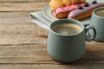 Aromatic coffee in cups, tasty eclairs and profiteroles on wooden table, space for text