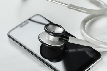 Modern smartphone and stethoscope on white table, closeup