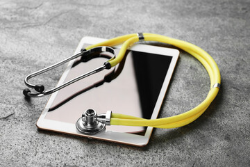 Modern tablet and stethoscope on grey table
