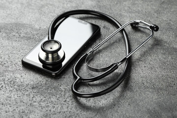 Modern smartphone and stethoscope on grey table
