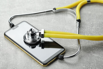 Stethoscope and modern smartphone on grey table