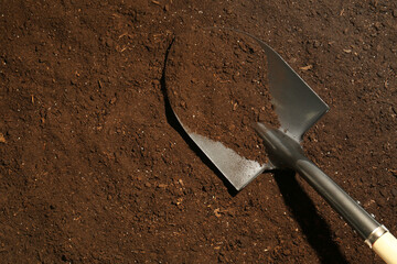 Metal shovel on fertile soil, top view and space for text. Gardening tool
