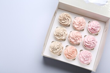 Tasty cupcakes in box on white background, top view. Space for text