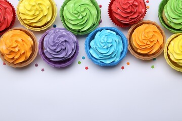 Many tasty cupcakes with bright cream and sprinkles on white background, flat lay. Space for text