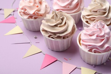 Delicious birthday cupcakes, sprinkles and bunting flags on violet background, closeup