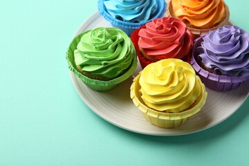 Plate with delicious bright cupcakes on turquoise background. Space for text