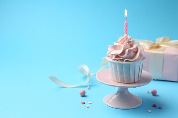 Delicious birthday cupcake with burning candle and sprinkles on light blue background, closeup....