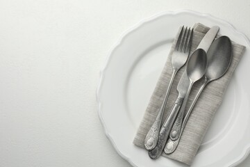 Stylish setting with cutlery and plate on white textured table, top view. Space for text