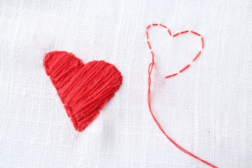 Embroidered red hearts and needle on white cloth, top view