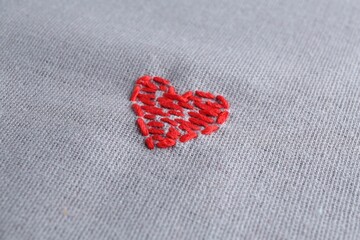 Fototapeta premium Embroidered red heart on gray cloth, closeup