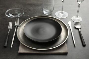 Stylish setting with cutlery, glasses and plates on black table
