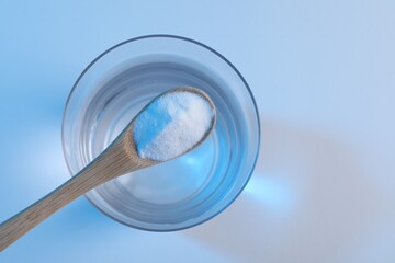 Spoon with baking soda over glass of water on light blue background, top view. Space for text