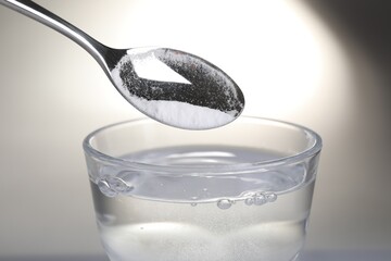 Adding baking soda into glass of water on light background, closeup