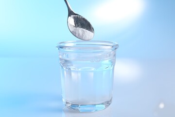 Adding baking soda into glass of water on light blue background