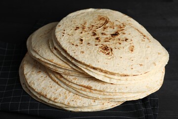Many tasty homemade tortillas on black wooden table, closeup
