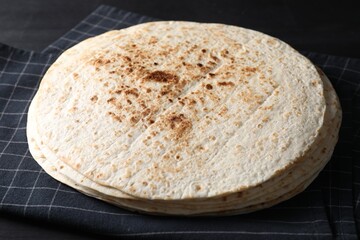 Many tasty homemade tortillas on black wooden table, closeup