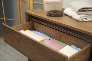 Chest of drawers with different folded clothes and accessories indoors