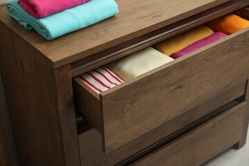 Wooden chest of drawers with different folded clothes indoors, closeup