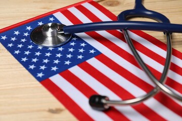 Stethoscope and USA flag on wooden table, closeup. Health care concept