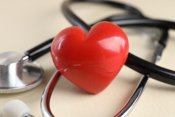 Stethoscope and red heart on beige background, closeup