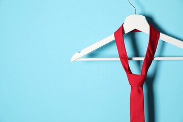 Hanger with red tie on light blue background. Space for text
