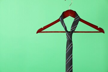 Hanger with black striped tie on green background. Space for text