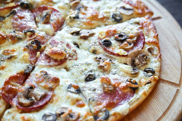 A detailed close-up showcasing the toppings of a pepperoni and mushroom pizza with black olives and melted cheese on a wooden surface