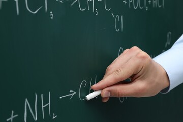 Teacher writing chemical formulas with chalk on green chalkboard, closeup