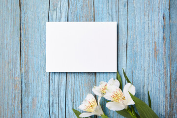 A landscape-oriented blank white card mockup on a weathered blue wooden surface, adorned by a spray...