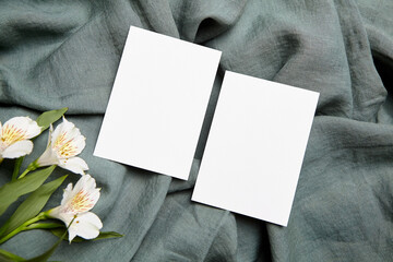 Two empty white cards displayed on a grey linen fabric, accompanied by white alstroemeria flowers...