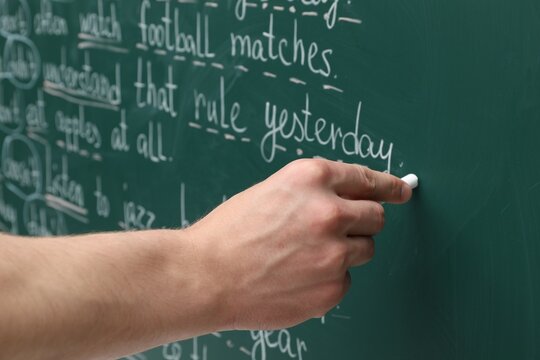 English teacher writing with chalk on green chalkboard, closeup
