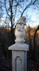 angel statue in the park. little boy with wings. cupid statue in autumn park. figurine for design, marble sad angel sitting on a ball. blurred natural background. 