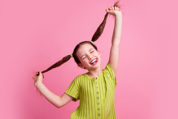 Photo portrait of lovely little girl pulling tails stick tongue dressed stylish green garment isolated on pink color background