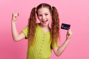Photo portrait of pretty little girl hold credit card winning wear trendy green outfit isolated on pink color background