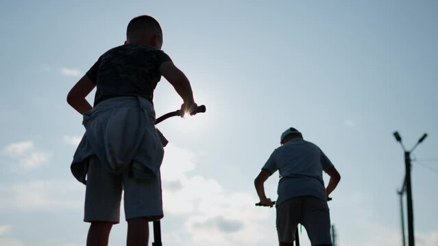 Teen scooterists ride around skatepark, performing extreme stunts.
