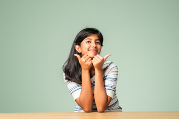 Happy Indian asian teenage girl showing or pointing something sitting at table