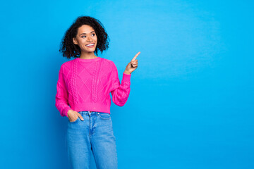 Photo of nice young girl look point finger empty space wear pink sweater isolated on blue color...