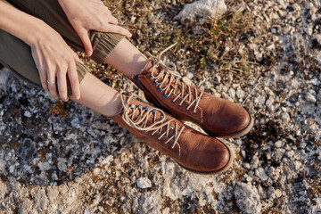 Woman's feet in brown boots resting on rocky surface with hands on knees in a serene moment of...