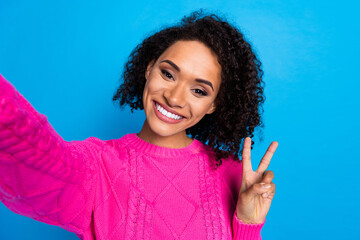 Photo of nice young girl make selfie show v-sign wear pink sweater isolated on blue color background