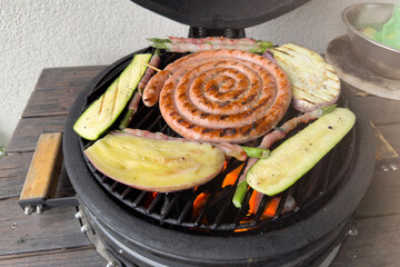 A man fries sausages and vegetables on the grill. Grilling season is open. Delicious grilled sausages close-up.