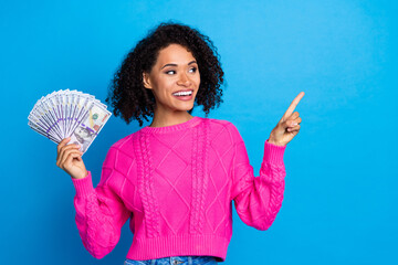 Photo of adorable pretty lady wear pink jumper rising dollars fan showing emtpy space isolated blue...