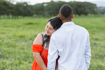 young latina woman smiling and hugging her boyfriend while leaning on his shoulder. man with his back turned.