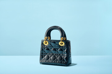Luxury Designer Black Quilted Handbag Purse with Gold Hardware on Blue two toned background